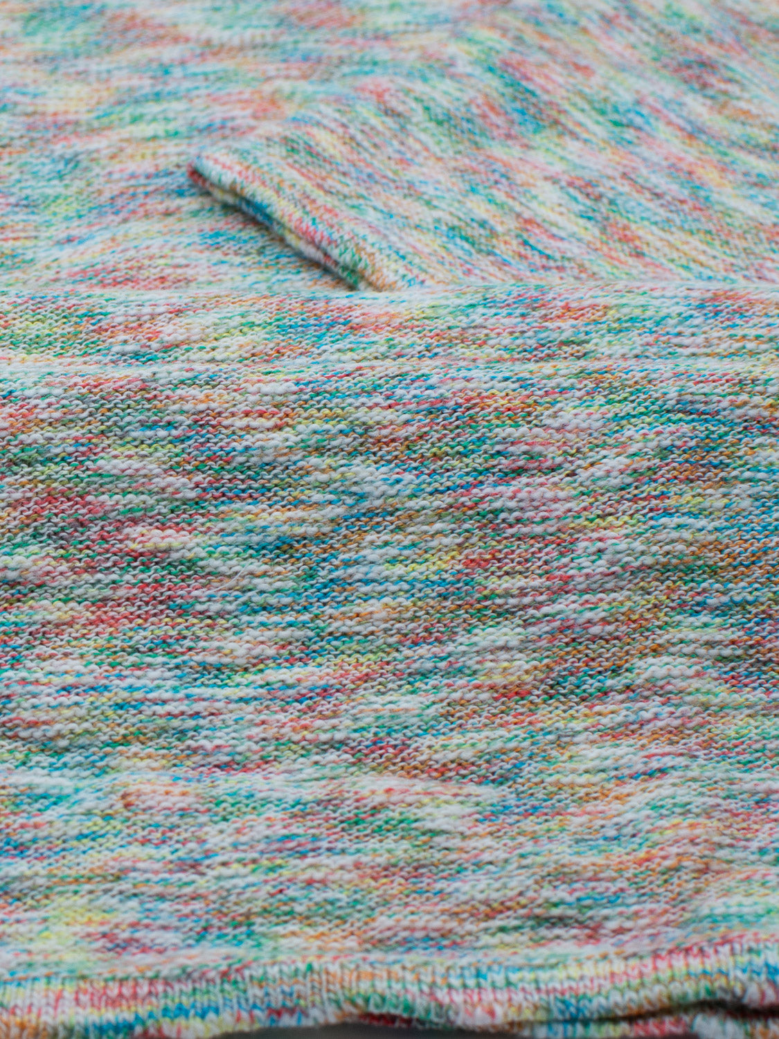 The Miami Reverse Knit Cotton Polo by ID Menswear showcases a breathable cotton-knit fabric with a soft, slightly fuzzy texture. Featuring multicolored patterns in blue, pink, yellow, and green with visible stitches and a small folded section at the top, it exudes casual wear charm.