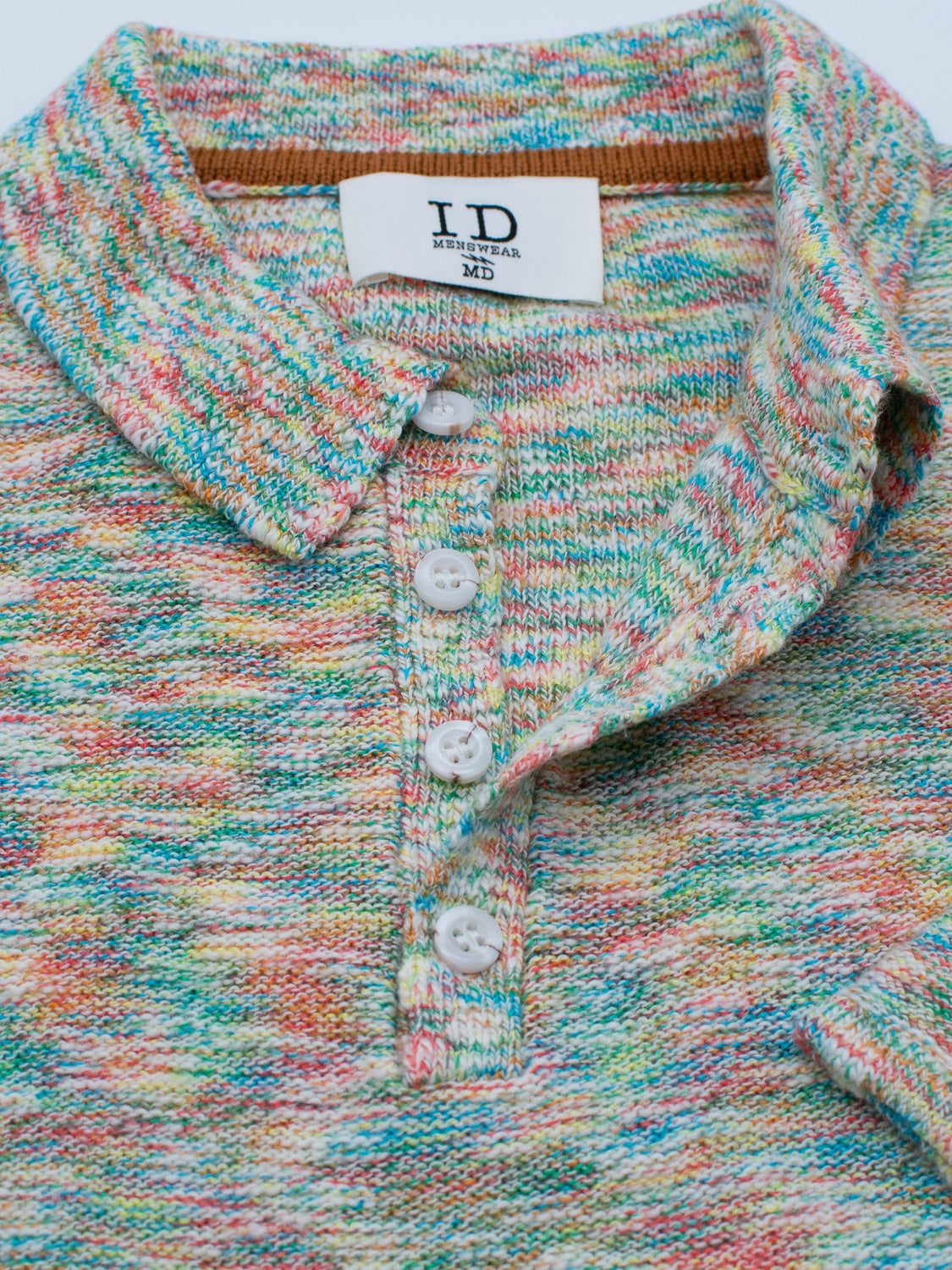 Close-up of the Miami Reverse Knit Cotton Polo by ID Menswear, featuring a multicolored speckled pattern. This casual polo has a collar, four white buttons, and an inside tag showing I.D. and Medium size for breathable everyday comfort.
