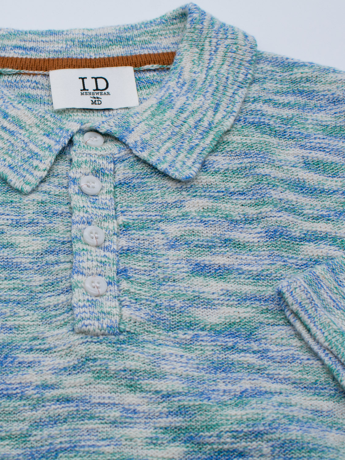 Close-up of the Miami Reverse Knit Cotton Polo by ID Menswear. This multicolored knit shirt features a breathable fit with blue, green, and white threads, a collar, brown inner lining, and four white buttons.