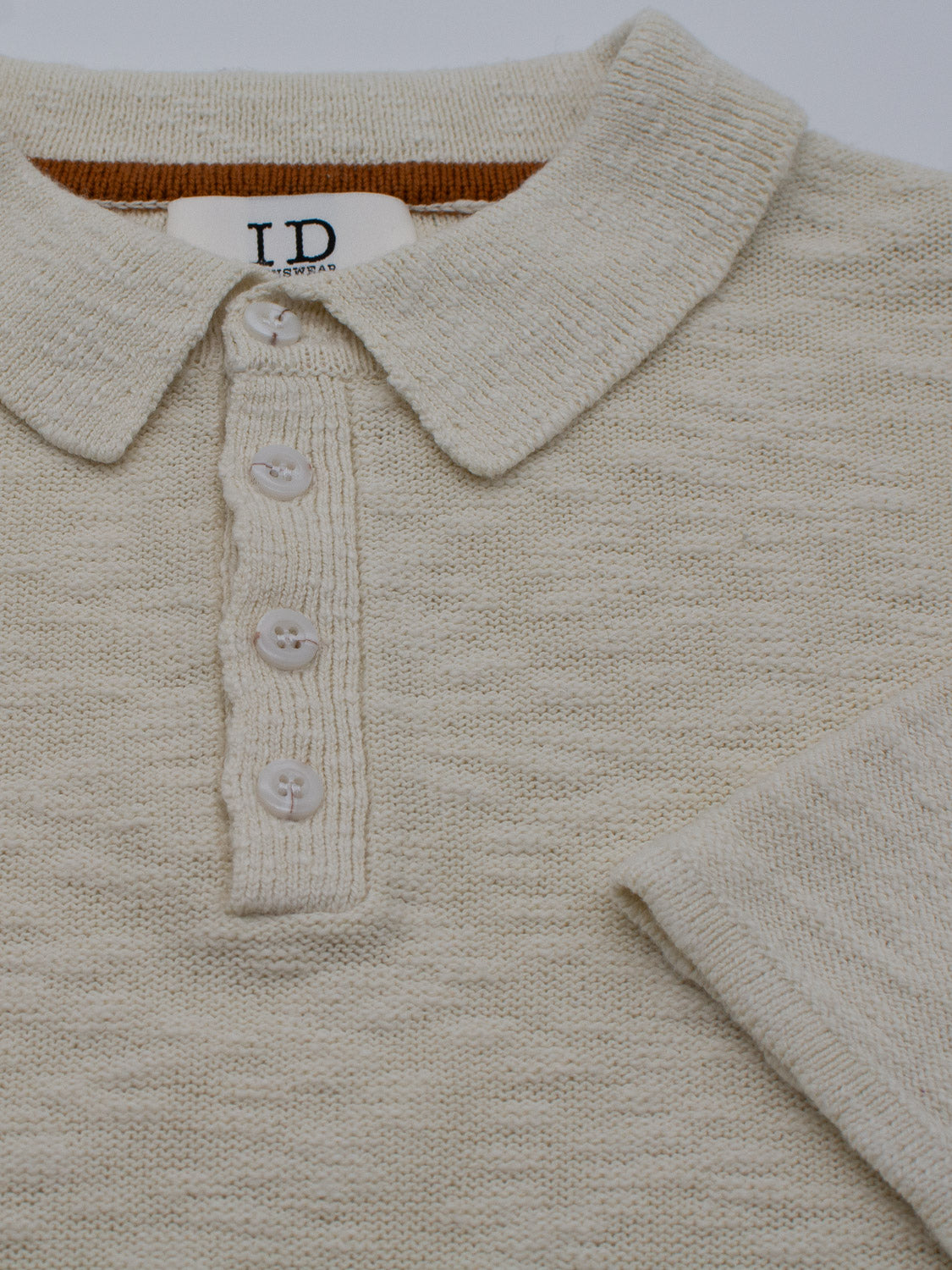 The Miami Reverse Knit Cotton Polo by ID Menswear is a light beige cotton-knit shirt featuring a collar and four buttons. Its breathable fit enhances texture. A label with LD is inside the collar, and one sleeve is partially visible on the right side, ideal for casual wear.