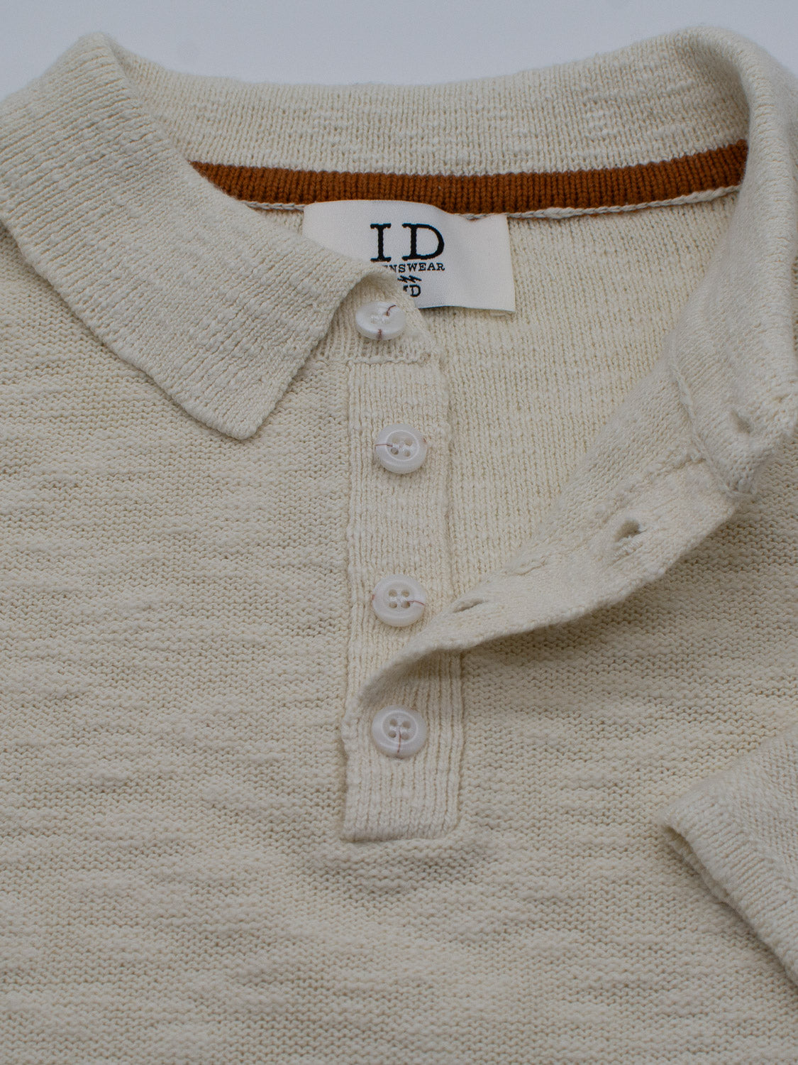 The Miami Reverse Knit Cotton Polo by ID Menswear is a beige knit cotton shirt featuring a textured fabric, three white buttons, a pointed collar with visible label, and an orange-brown stripe. Its breathable, ideal for casual wear.