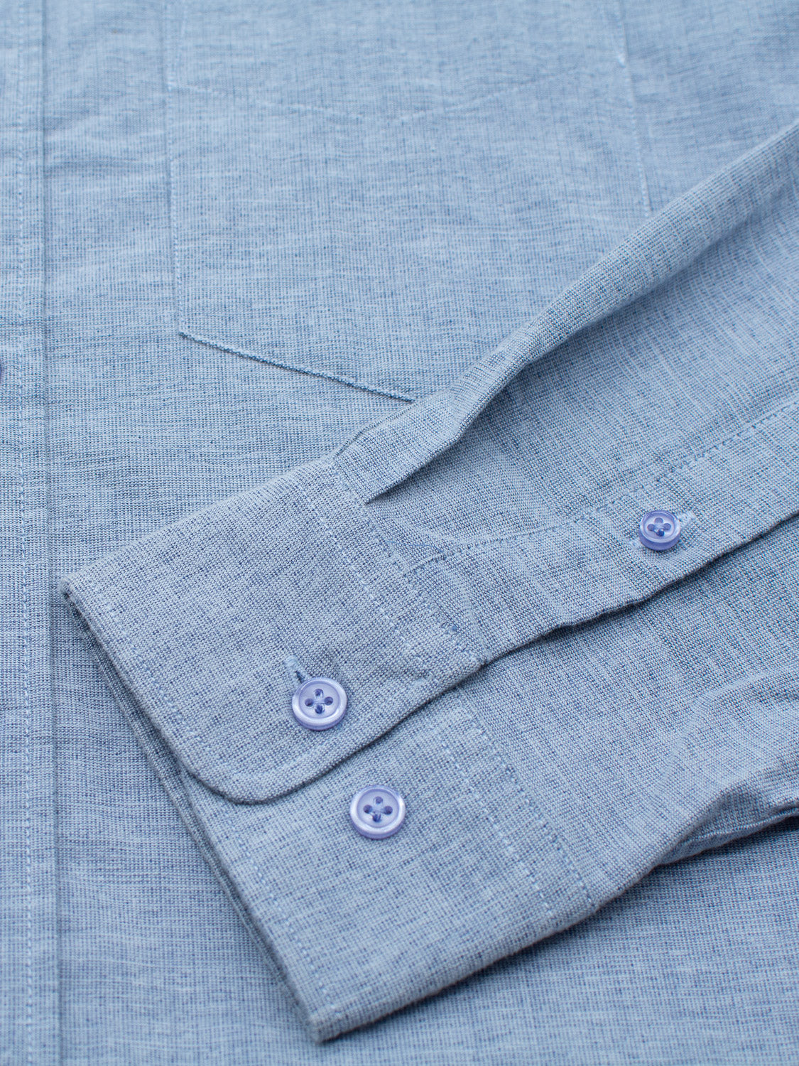 Close-up of the Akira Cotton Button Down Shirt by ID Menswear in light blue. Focus is on the left sleeve with two blue buttons on the cuff. The soft, finely woven fabric has subtle grid patterns that highlight its classic regular-fit style.