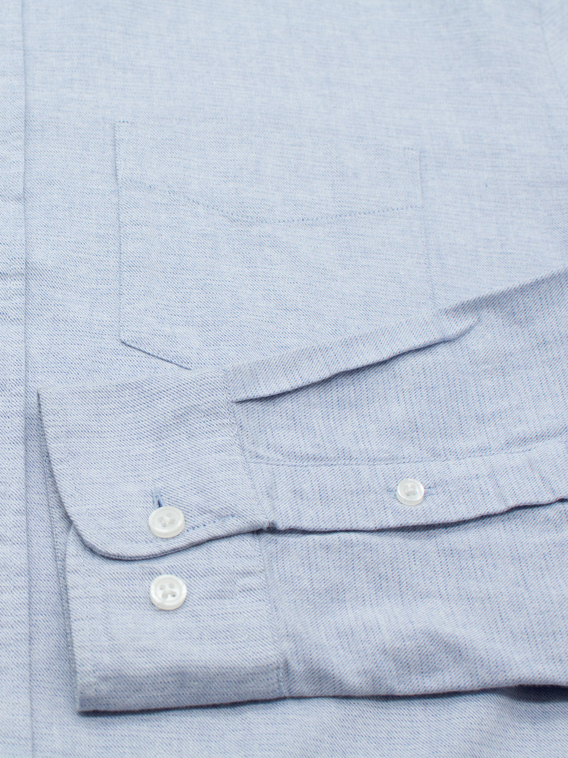 Close-up of the Akira Cotton Button Down Shirt by ID Menswear in light blue. It features textured fabric, a visible chest pocket, and folded sleeves. The design is completed with two white cuff buttons for a classic touch to this regular-fit shirt.