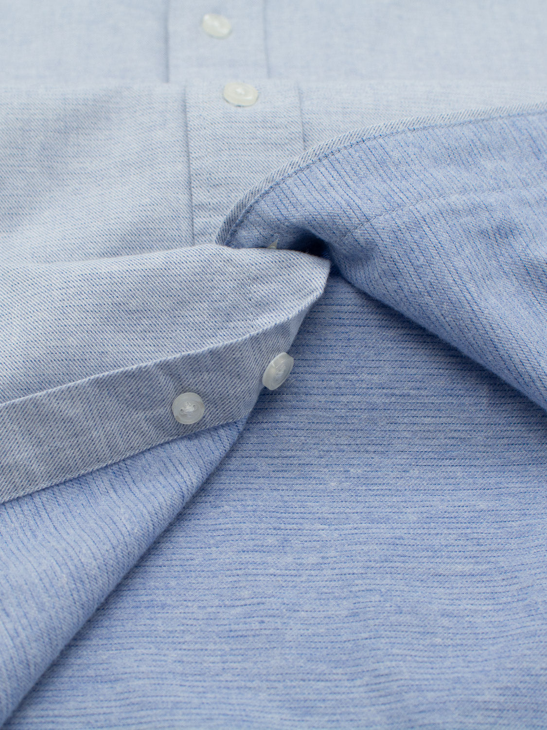 Close-up of the Akira Cotton Button Down Shirt by ID Menswear in light blue. The regular-fit, textured fabric features a buttoned cuff, with the shirt partially folded to reveal the inside.