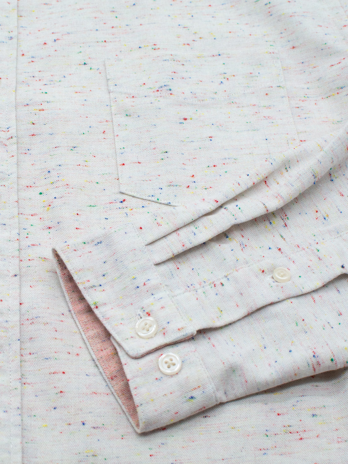 Close-up of an ID Menswear Allswell Speckled Button Down Shirt in premium cotton-linen with multicolored dots. A pocket and buttoned cuff highlight its versatile design and texture.