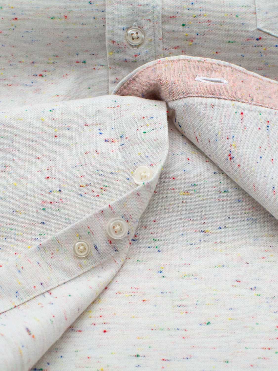 Close-up of the Allswell Speckled Button Down Shirt by ID Menswear, crafted from a premium cotton-linen blend. Featuring a versatile speckled pattern in blue, red, and yellow, this shirt is partially unbuttoned to reveal its inner material and finished with classic white buttons.