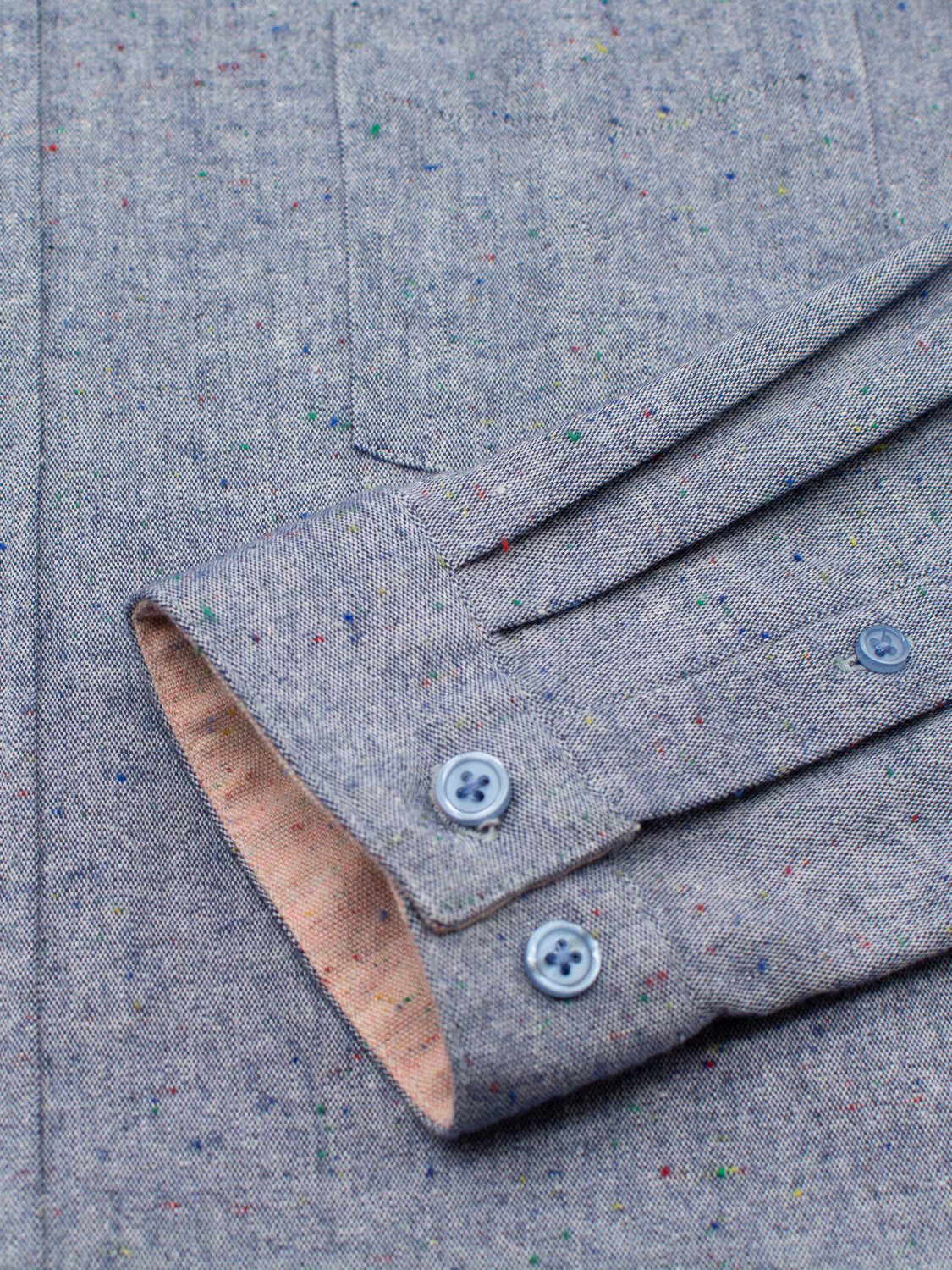 Close-up of an ID Menswear Allswell Speckled Button-Down Shirt sleeve in a premium cotton-linen blend, featuring colorful dots, two blue buttons, and cuff pleats. The contrasting beige lining inside adds extra charm.