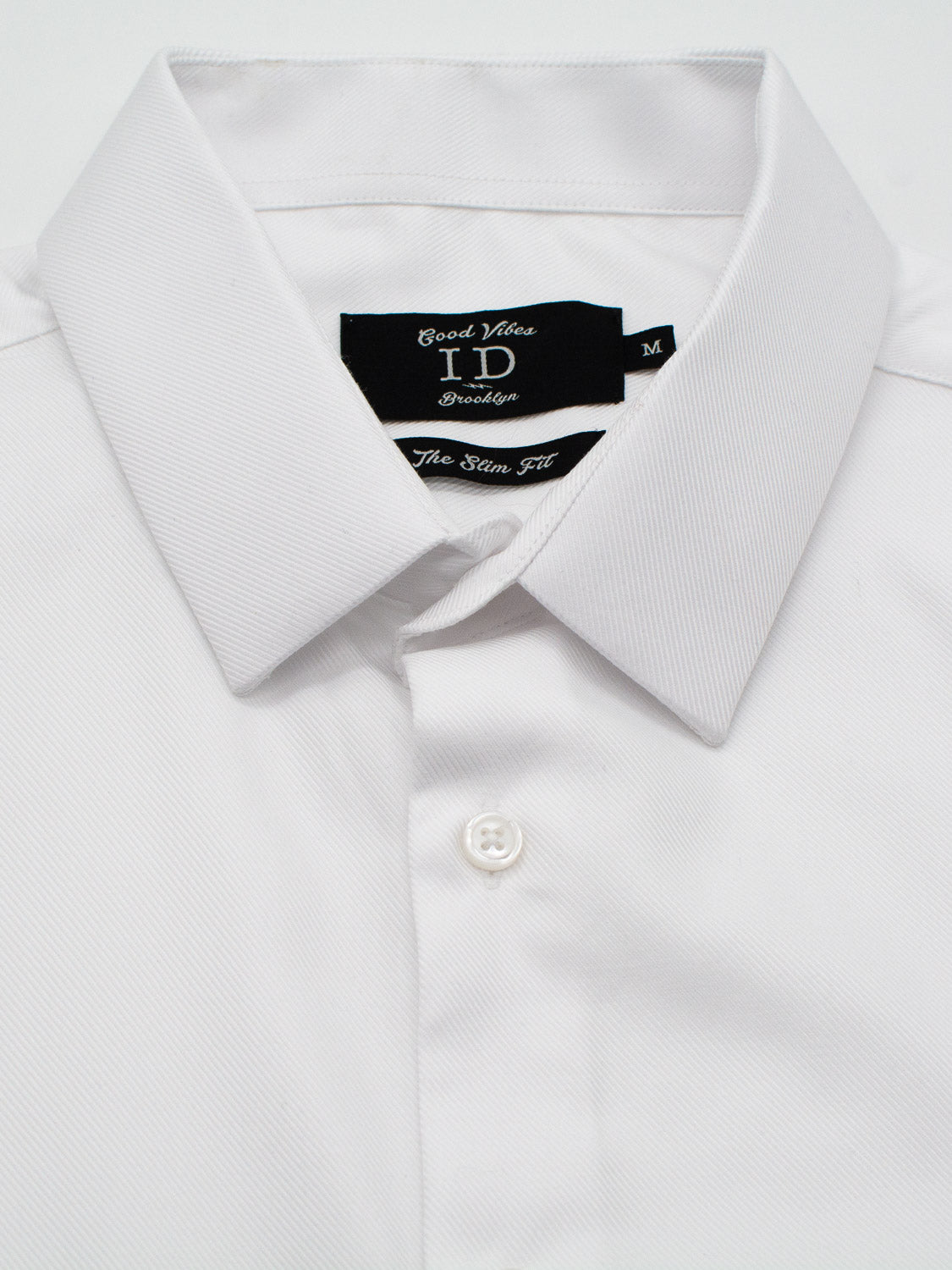 A neatly folded white Cotton Dress Shirt in Slim Fit by ID Menswear features a pointed collar and a visible white button at the bottom. Inside the collar, the black label reads "ID Menswear, The Slim Fit.