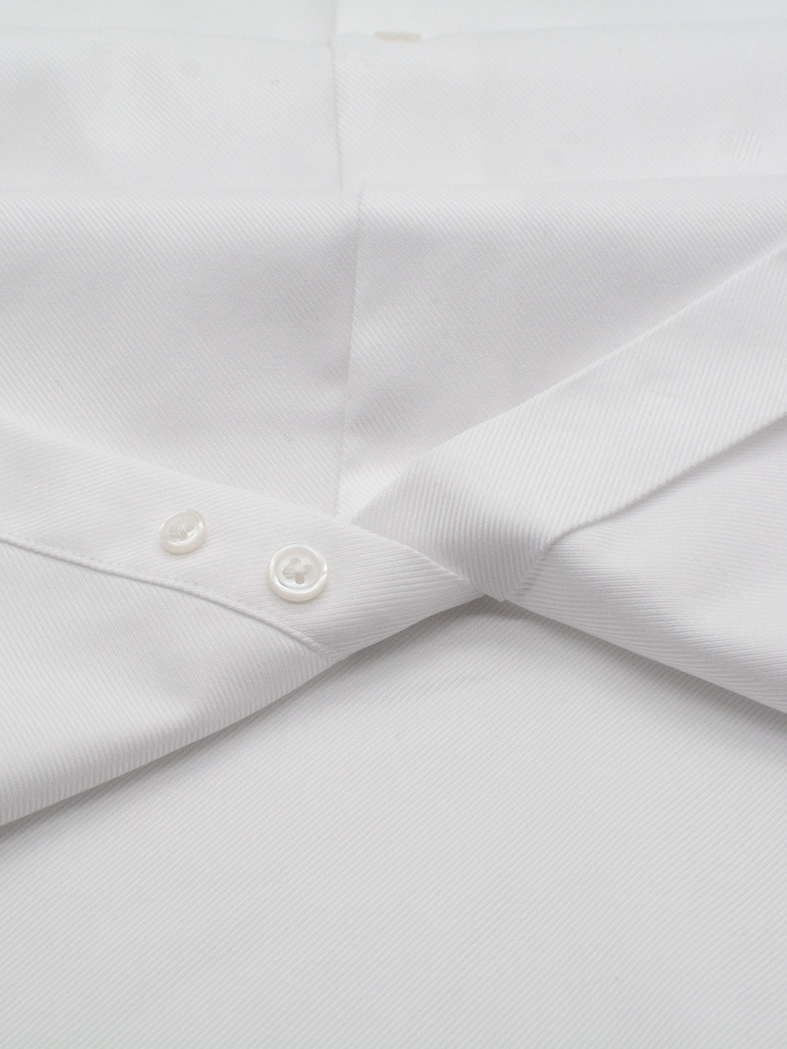 A close-up of the ID Menswear Cotton Dress Shirt in Slim and Regular Fit shows its white collar and buttons on a white surface, with a subtle diagonal weave that enhances the shirt’s refined, tailored look.