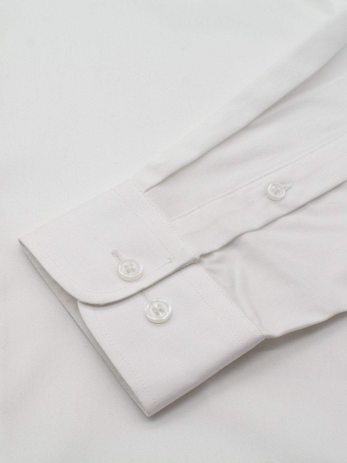 Close-up of a white ID Cotton Dress Shirt from ID Menswear in slim fit, featuring a smooth fabric and neatly stitched cuff with two button closures on a light background.