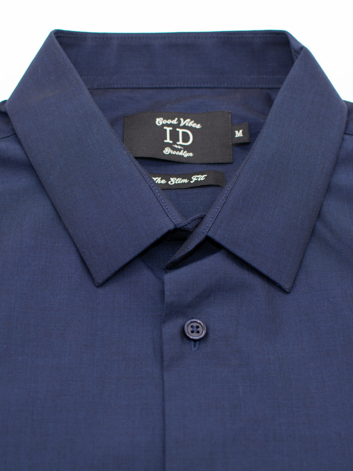 A close-up of a neatly folded dark blue Cotton Dress Shirt in Slim Fit with a pointed collar. The inside black label features ID Menswear and the size M is visible.