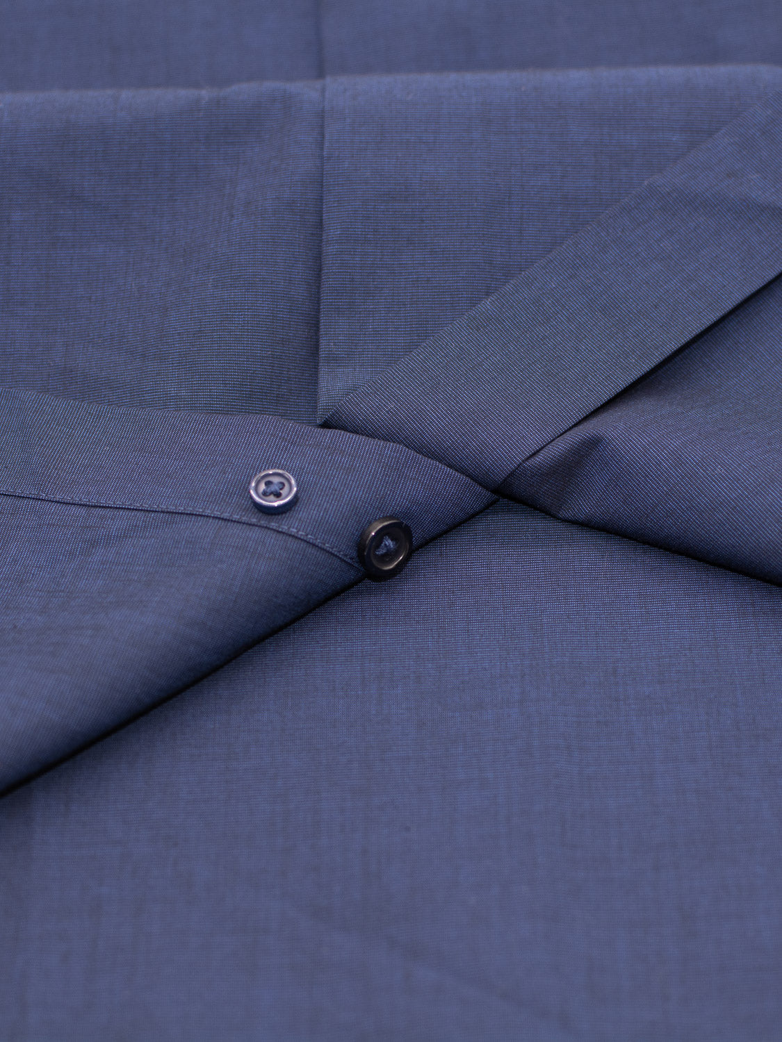 A close-up of the Cotton Dress Shirt by ID Menswear in Slim and Regular Fit shows two dark blue buttons near a folded seam, highlighting the texture and weave of the fabric.