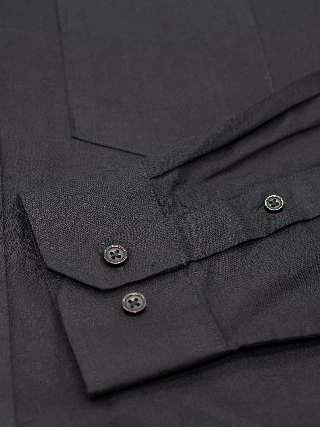 Close-up of a dark Goa Linen Cotton Long Sleeve Shirt by ID Menswear with folded sleeves, showcasing two black-button cuffs and smooth, lightweight fabric with detailed edge stitching.