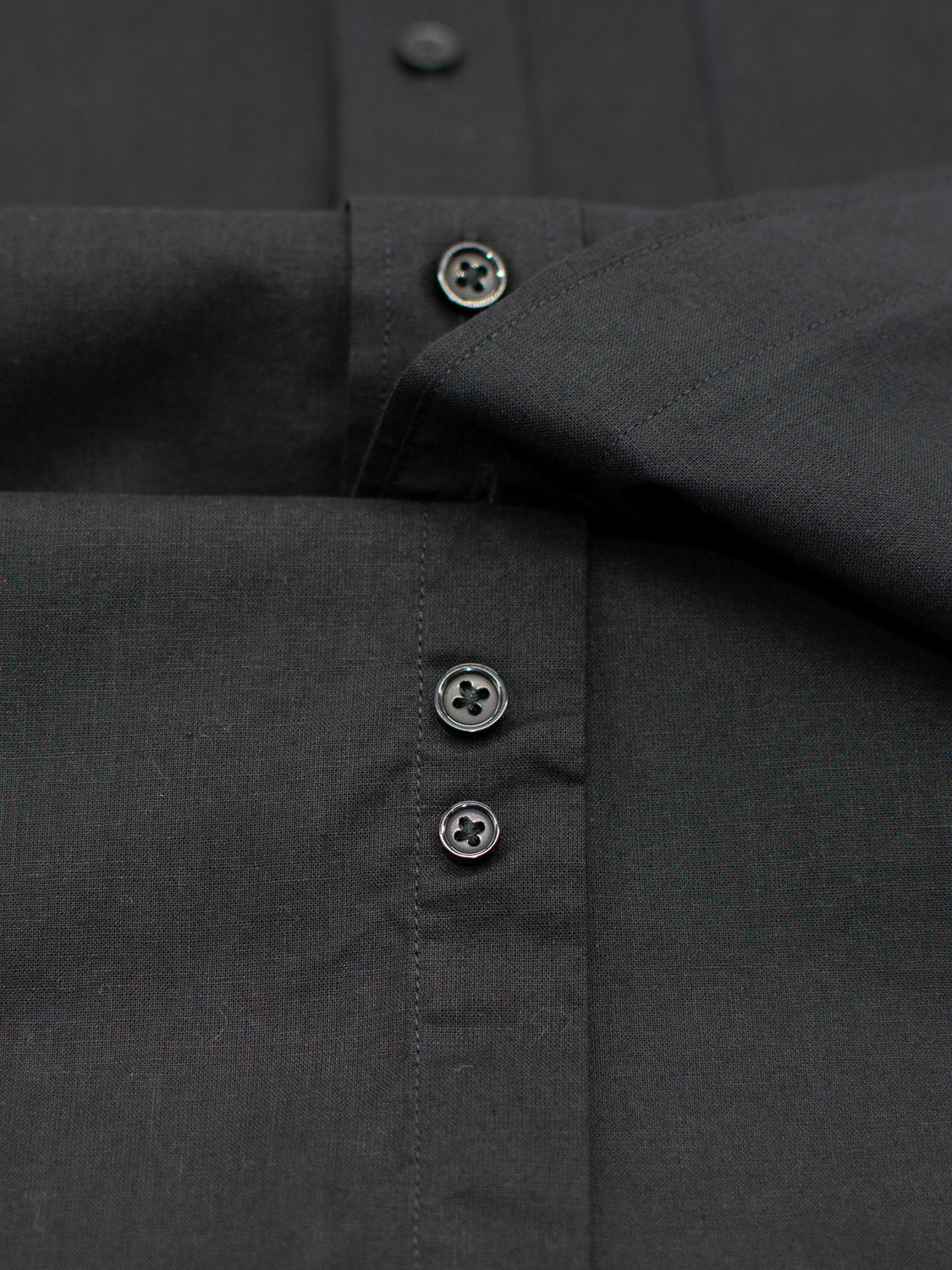 Close-up of ID Menswears Goa Linen Cotton Long Sleeve Shirt, crafted from smooth, breathable fabric. The black dress shirt features a front button placket with three black buttons, and is neatly folded to showcase its details.