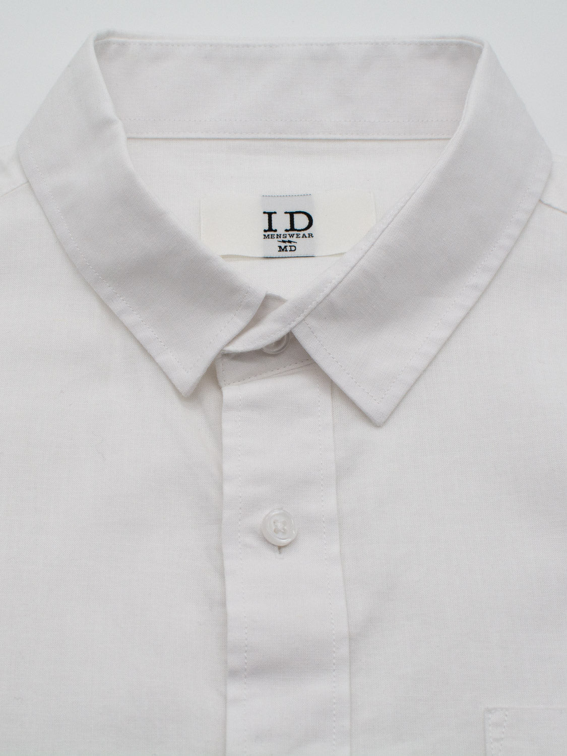 A close-up of a lightweight, white Goa Linen Cotton Long Sleeve Shirt with a collar is laid flat on a white surface. The inside label from ID Menswear reads ID and Medium in black text.