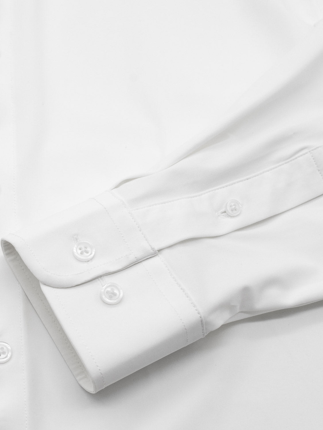 Close-up of an Axel 4-Way Stretch Dress Shirt by ID Menswear, spotlighting the sleeve and buttoned cuff with two white buttons, subtly showing the main body in the background. This white slim-fit shirt promises comfort for any occasion.