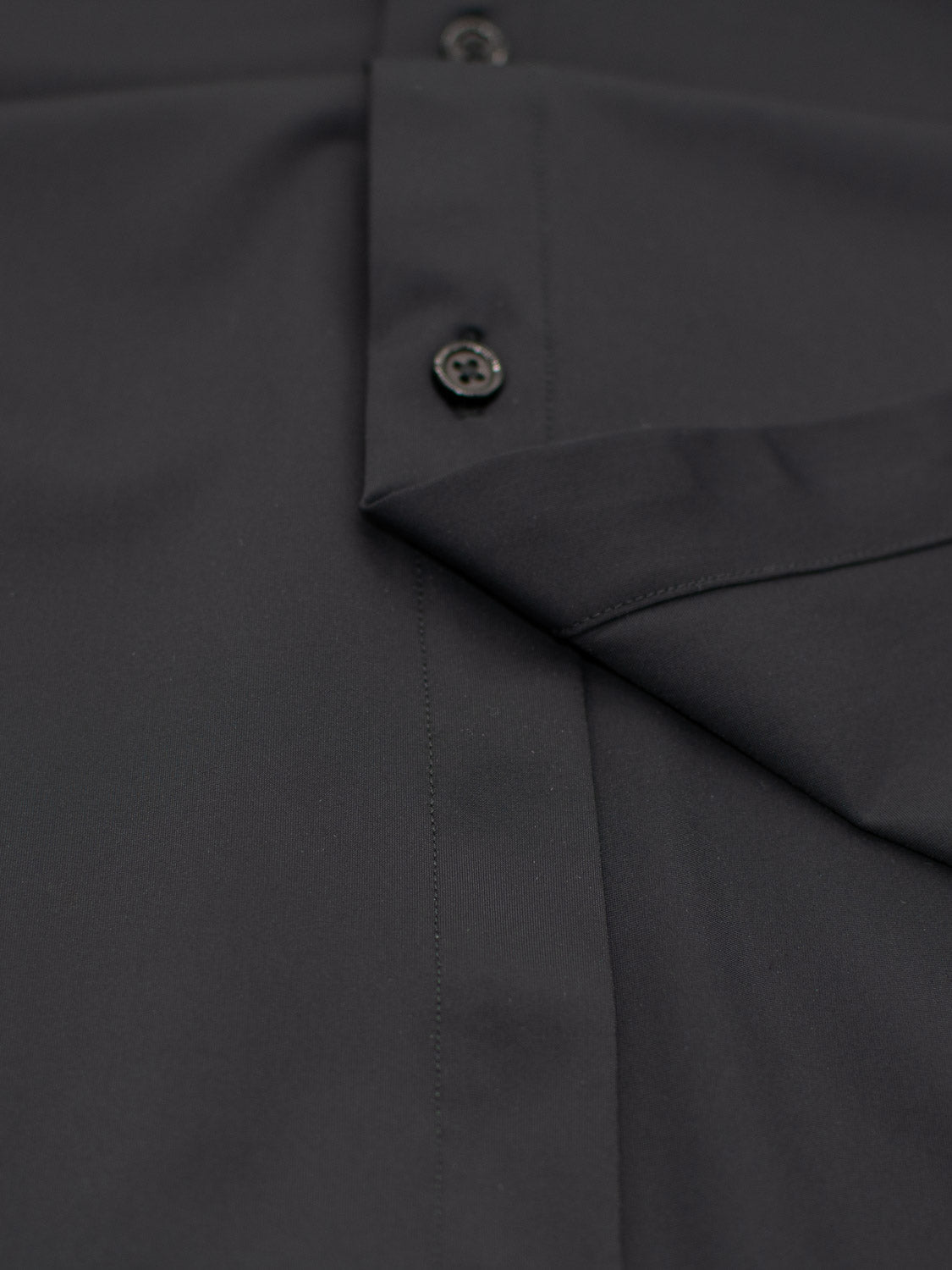 Close-up of the Axel 4-Way Stretch Dress Shirt by ID Menswear, highlighting three sleek black buttons and a neatly sewn hem. The smooth, finely stitched fabric offers comfortable wear.