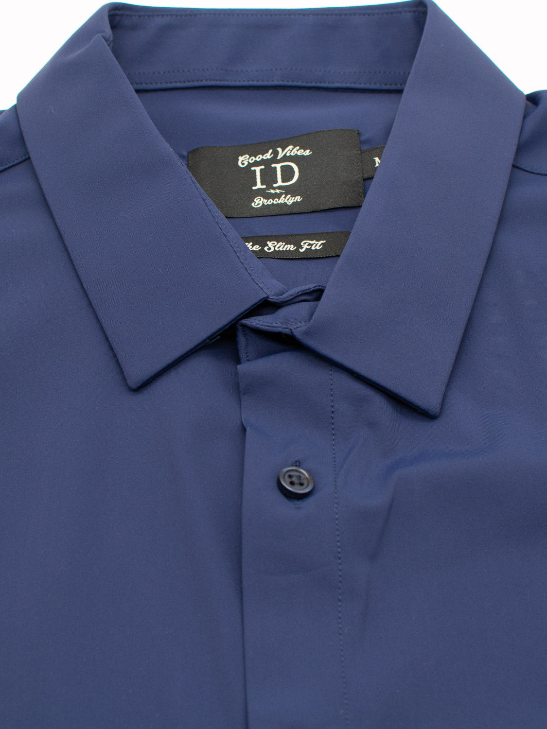 A close-up of a neatly folded Axel 4-Way Stretch Dress Shirt in dark blue by ID Menswear, featuring a collar. The tag reads Brooklyn, The Slim Fit. This comfortable shirt lies buttoned up and flat on a white surface.