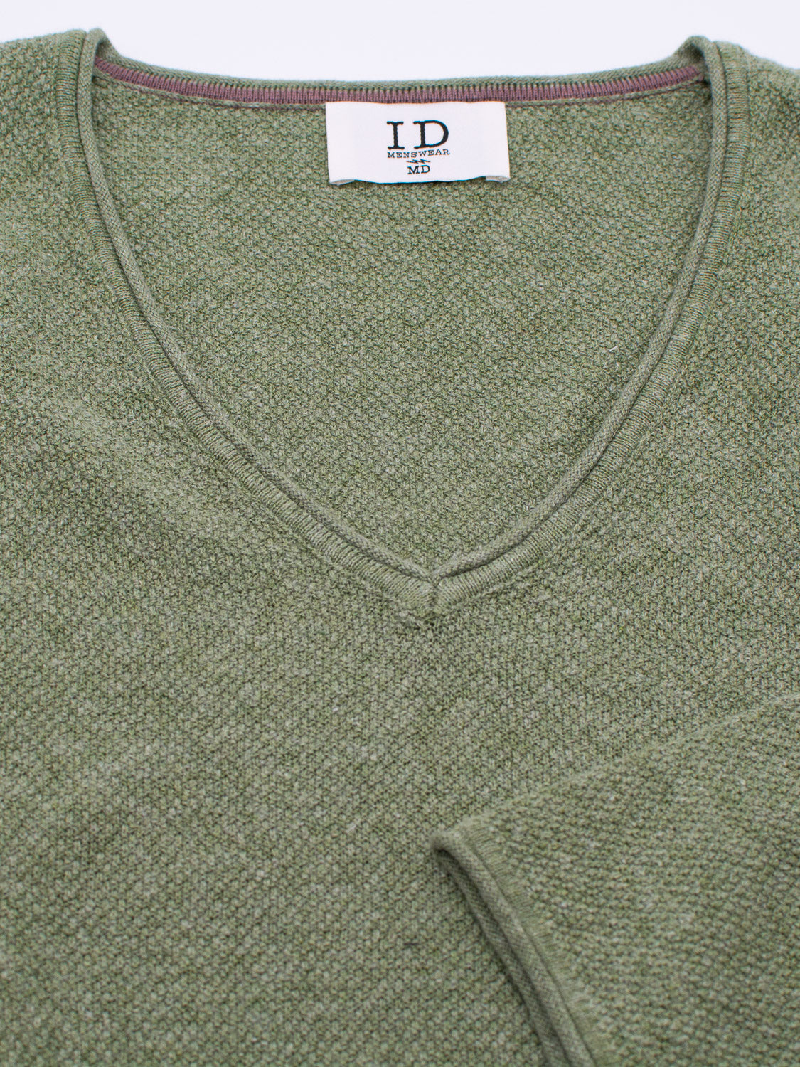 Close-up of an Amalfi Deep V Knitted Top by ID Menswear, showcasing the textured green linen-cotton blend with a visible ID MENS WEAR M3 label at the collar and a partial sleeve that highlights the fabrics texture.