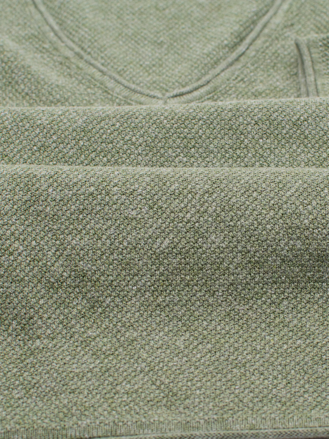 A close-up of folded green knit fabric from the Amalfi Deep V Knitted Top by ID Menswear highlights its texture and weave. The neat layers suggest a deep V-neck design.
