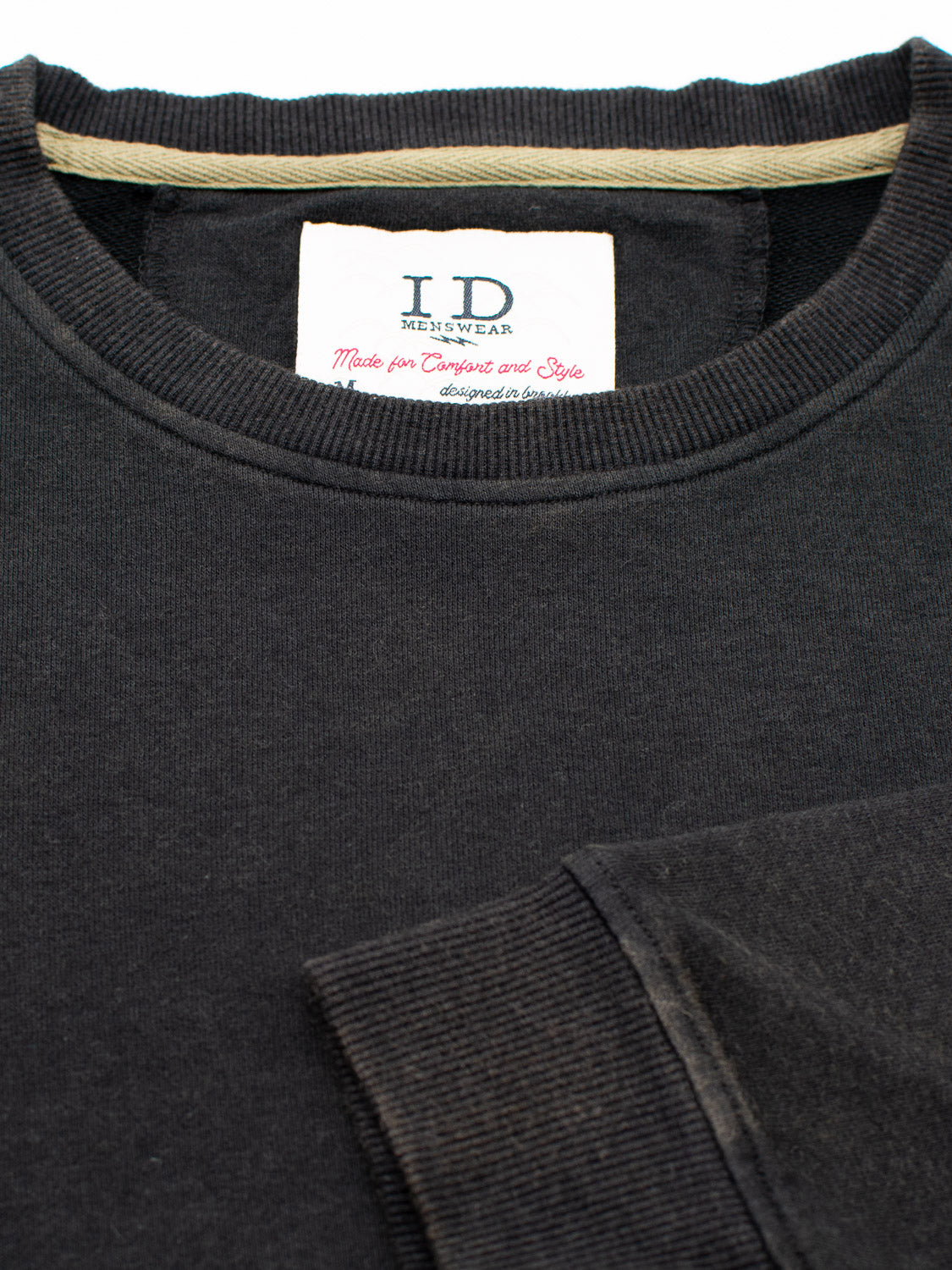 Close-up of a black Champ Bamboo Organic Cotton Sweatshirt by ID Menswear, featuring a neck label that reads Made for Comfort and Style in red and black text. The ribbed neckline and sleeve cuffs enhance its appeal.