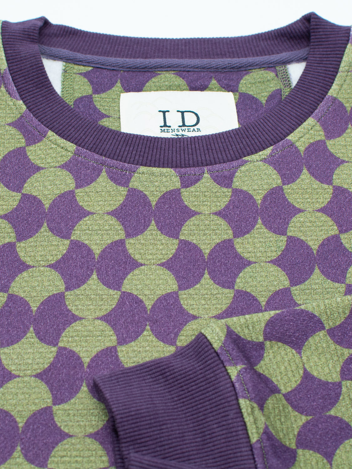 A close-up of the Wiggle Geometric Printed Sweatshirt in bamboo cotton fleece shows a green design with purple circular patterns and ribbed cuffs. The white ID Menswear label adds a casual touch.