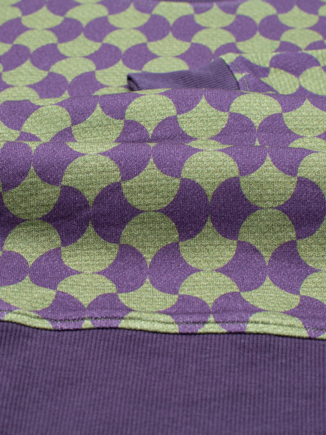 A close-up of bamboo cotton fleece with overlapping purple and light green circles shows a partly folded solid purple section, ideal for crafting the Wiggle Geometric Printed Sweatshirt by ID Menswear.