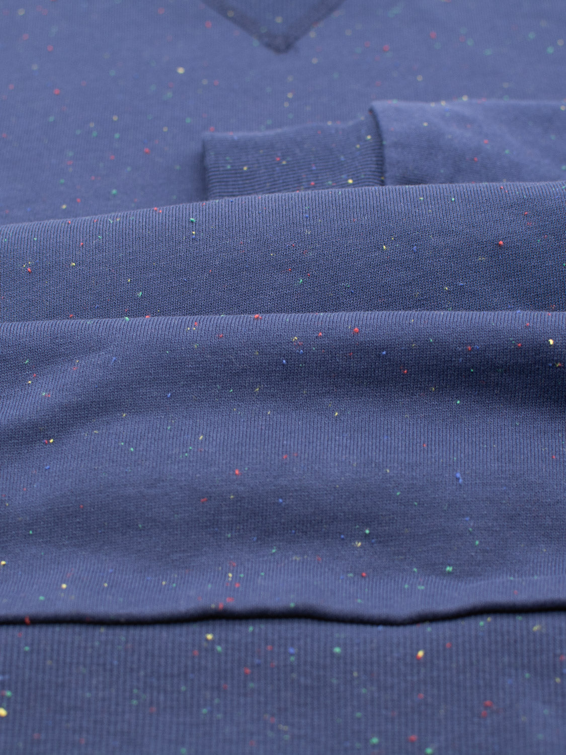 The Stardust Speckled Sweatshirt by ID Menswear features a blue cotton yarn fabric, adorned with colorful speckles reminiscent of stardust. A close-up reveals its texture and slight folds, showcasing its regular fit design.