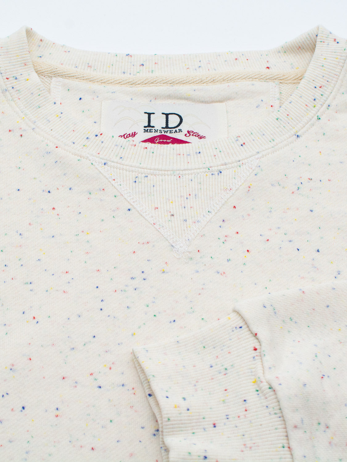 Close-up of the Stardust Speckled Sweatshirt by ID Menswear, featuring colorful dots. The visible neckline and sleeve are crafted from speckled cotton yarn for enhanced texture and design.