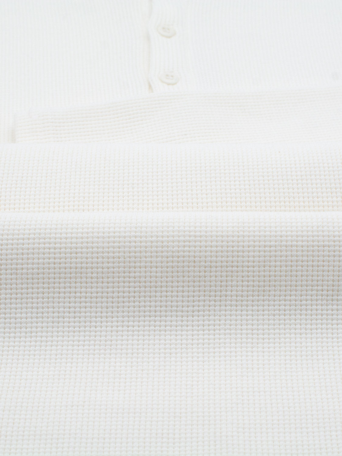 Close-up of ID Menswears Freestyle Waffle Knit Henley, displaying its white textured fabric with a waffle pattern and buttons along the top edge. The fabric is neatly folded to highlight its woven texture and subtle design.