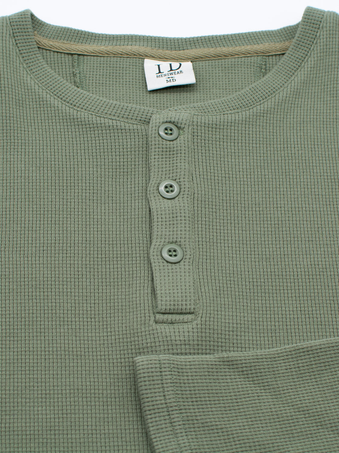 A close-up of the ID Menswear Freestyle Waffle Knit Henley in green highlights its regular fit and round neckline with a four-button placket. Made from a cotton-spandex blend for comfort, it features an inside beige care tag and a prominently displayed textured pattern.