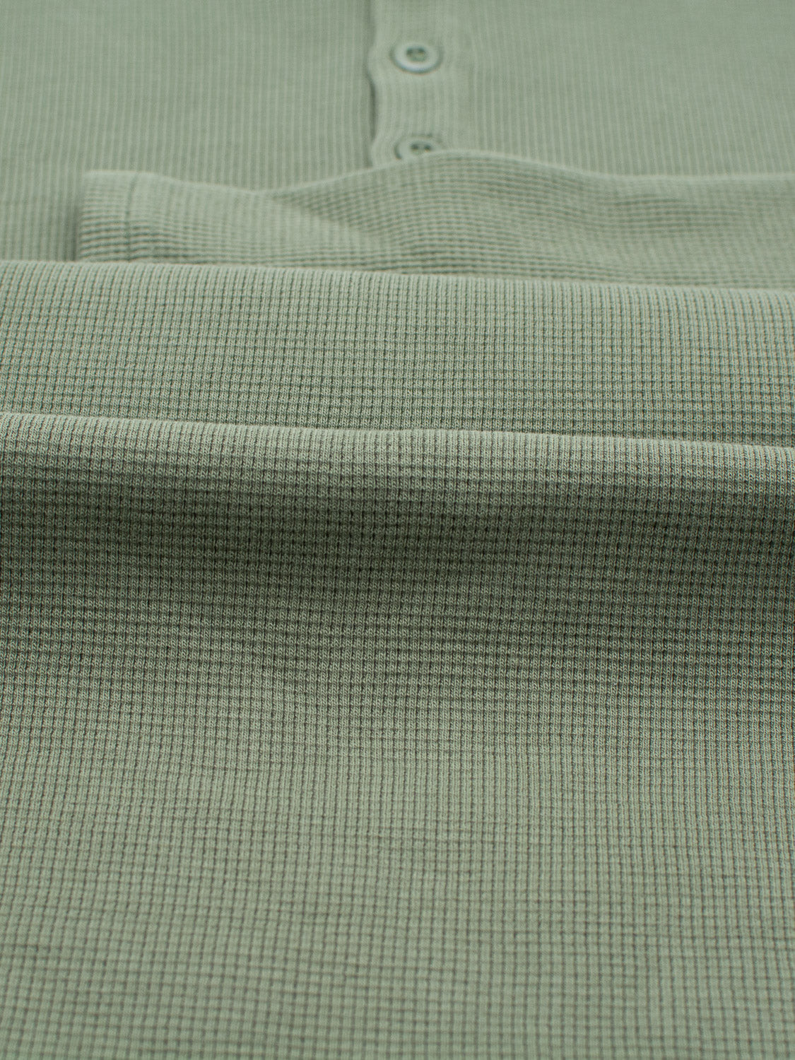 Close-up of a textured, light green Freestyle Waffle Knit Henley by ID Menswear, showcasing a cotton-spandex blend with a subtle grid and three buttons on the placket, highlighting its refined regular fit style.
