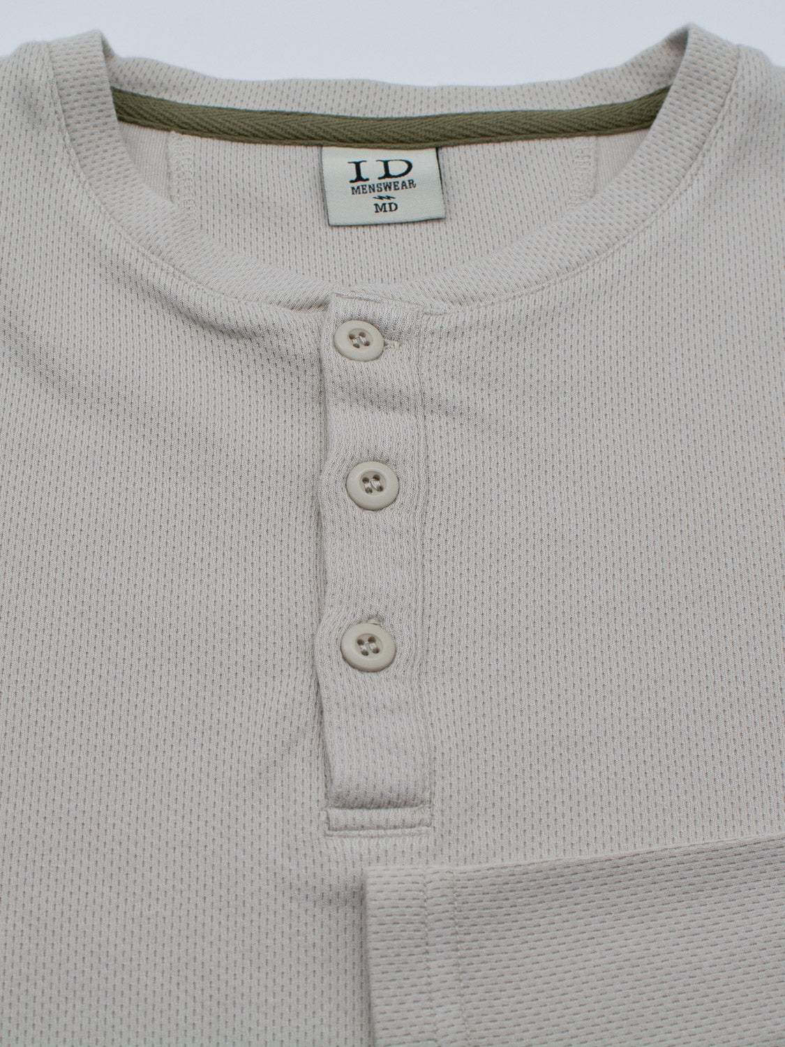 Close-up of the ID Menswear Freestyle Honeycomb Knitted Mesh Henley, a light beige textured organic cotton shirt with a three-buttoned placket. A visible tag inside the collar reads ID Menswear MD.