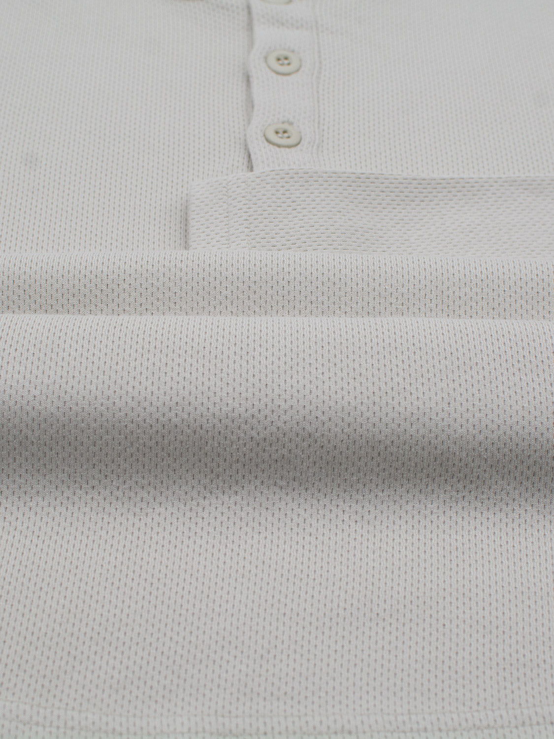 Close-up of ID Menswears Freestyle Honeycomb Knitted Mesh Henley, a light gray shirt with a honeycomb texture and two-button placket showcasing its casual comfort.