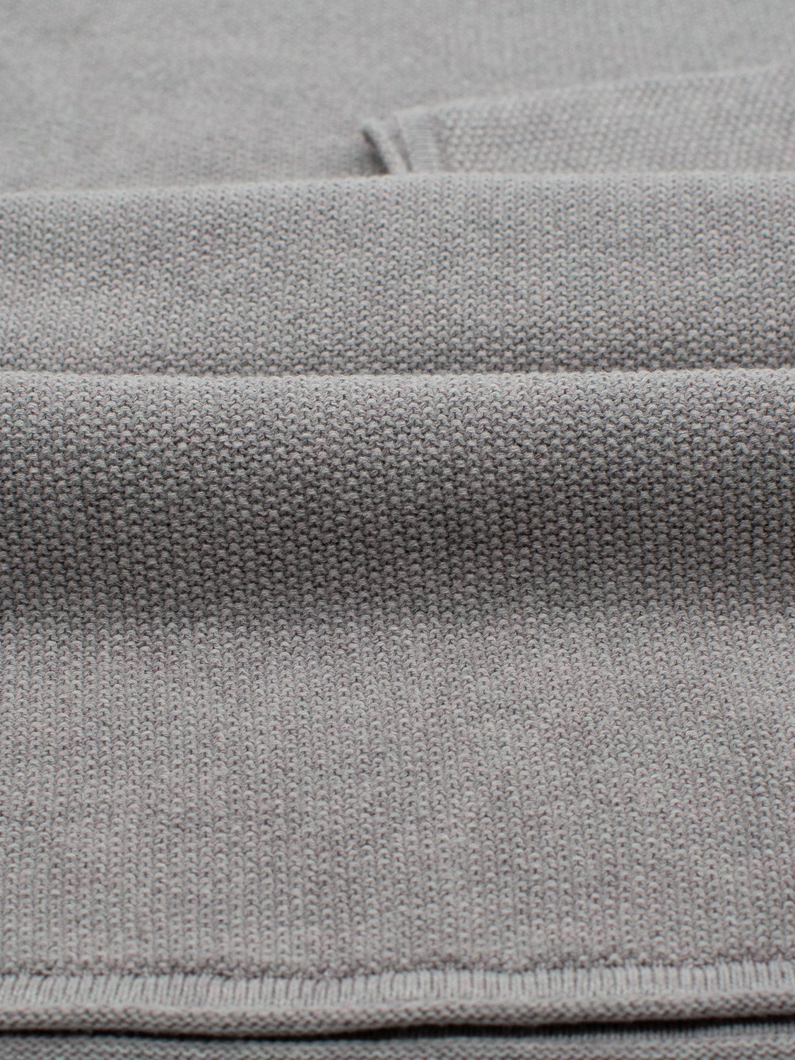 Close-up of the Madrid Rolled Neck Sweater Tee by ID Menswear, showcasing its lightweight gray knit fabric with a mini popcorn pattern. Gentle folds highlight the materials flexibility and warmth.