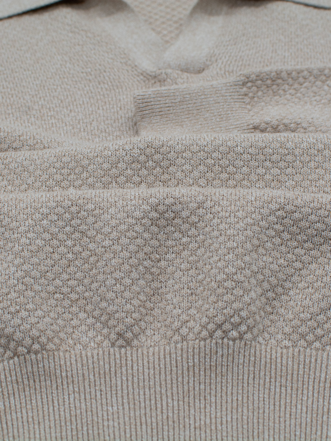 Close-up view of a folded beige knitted sweater with a collar, ideal for smart-casual occasions. The fabrics texture and subtle shadowed folds give it the look of the Seattle Long Sleeve Cotton Polo by ID Menswear.