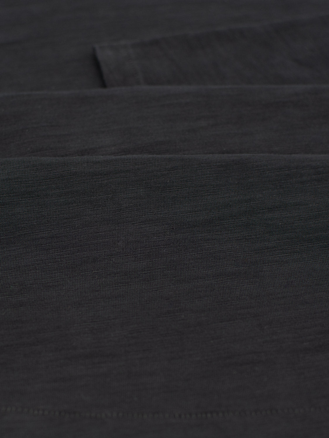 A close-up of dark gray, smooth slub cotton showcases its texture and faint shadows, suggesting a folded or draped surface—ideal for crafting the Paradise Long Sleeve Tee by ID Menswear, epitomizing casual wear.