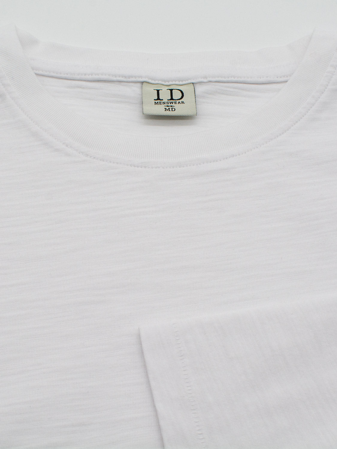 Close-up of the Paradise Long Sleeve Tee by ID Menswear, featuring its plain white Slub Cotton texture. Casually folded, its simple design is ideal for casual wear, with a visible brand tag ID MENSWEAR MD.