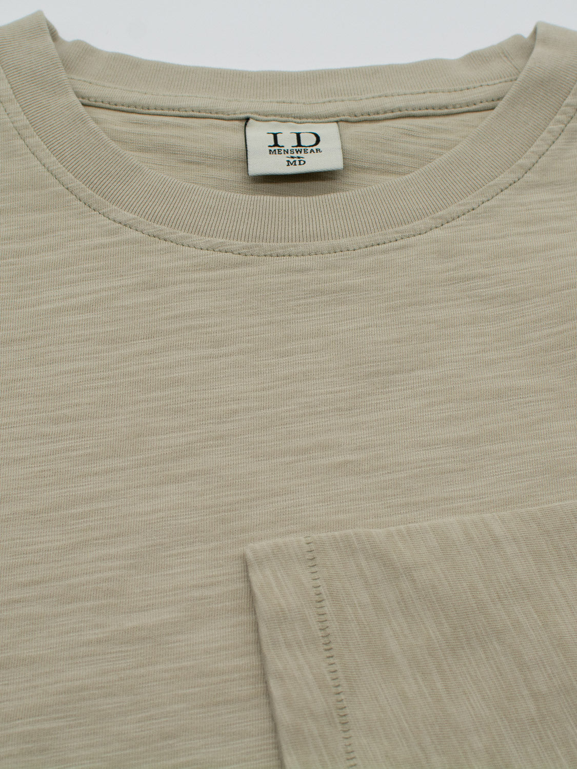 Close-up of a beige slub cotton Paradise Long Sleeve Tee with a round neckline and a bottom right pocket. The collar label reads ID Menswear M, highlighting its subtle textured pattern ideal for casual wear.