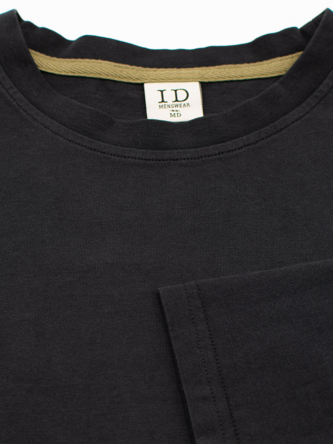 Close-up of the Sublime Long Sleeve Tee in black organic cotton by ID Menswear, featuring a beige neck lining and label. The visible sleeve highlights its casual appeal.