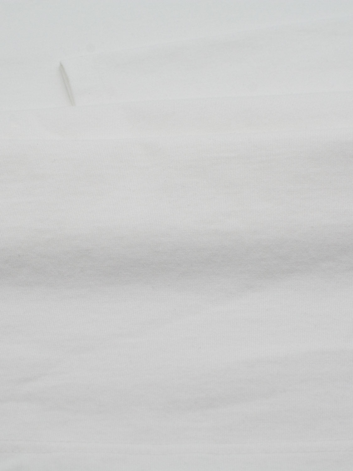 Close-up of a plain white fabric with subtle horizontal creases from the ID Menswear Sublime Long Sleeve Tee. The texture seems soft and smooth, with gentle shadows highlighting the folds, ideal for casual wear.