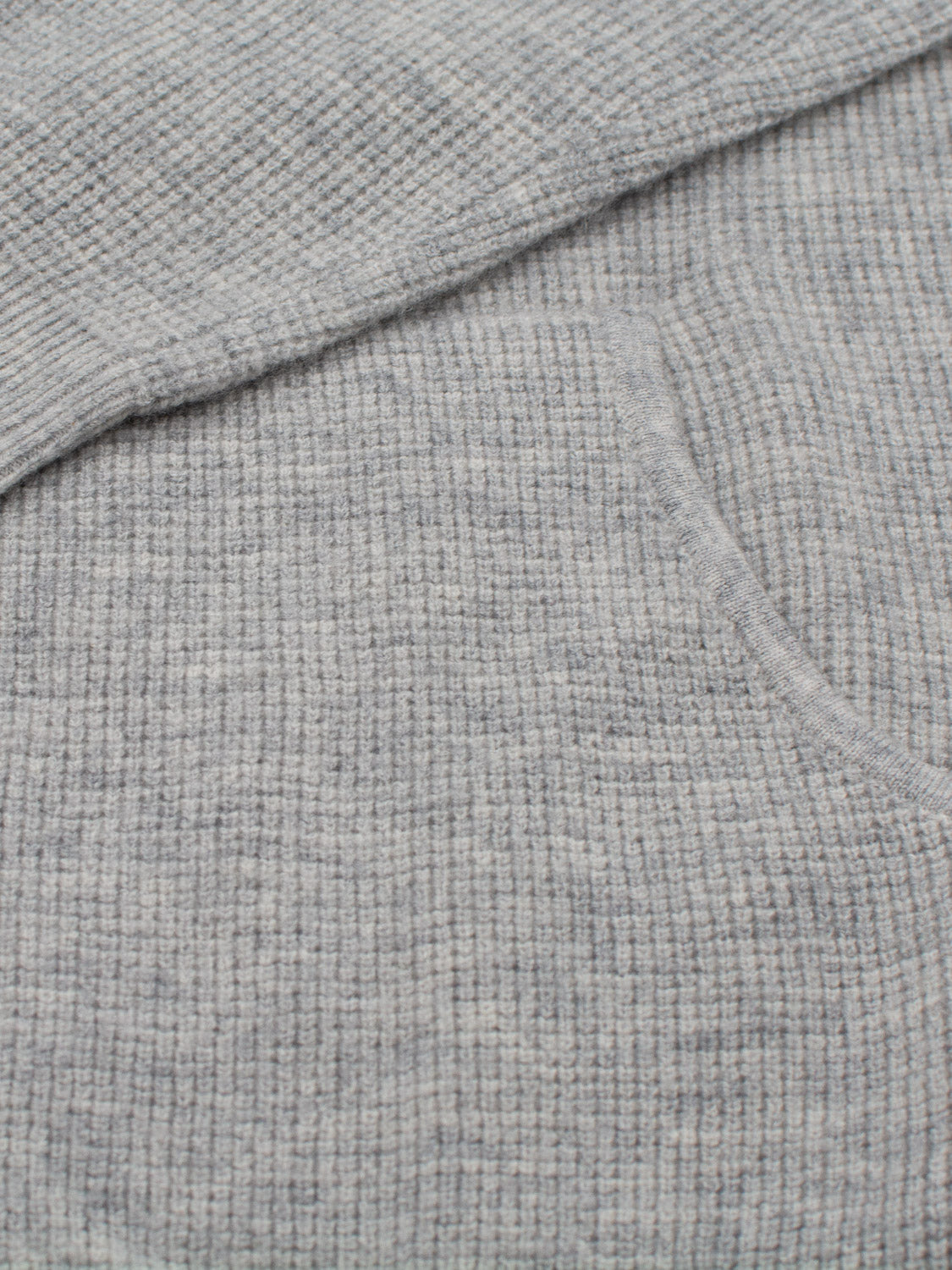 Close-up of gray ribbed fabric with subtle texture and visible seam featuring pocket detail, likely part of the cozy Bergen Waffle Knit Merino Hoody from ID Menswear. The exquisitely soft fabric suggests luxurious merino wool craftsmanship.