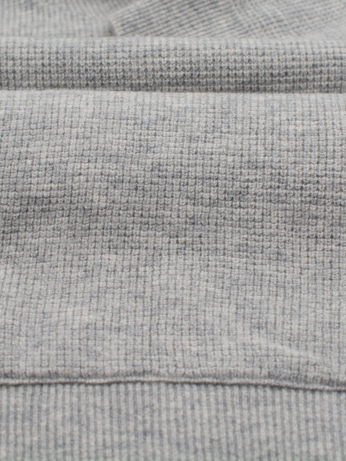 Close-up of ID Menswears Bergen Waffle Knit Merino Hoody, showcasing gray merino wool with a subtle grid pattern. The soft, raised lines form a gentle checkered design, reminiscent of waffle knit, and the fabric is slightly folded to reveal its depth and texture.