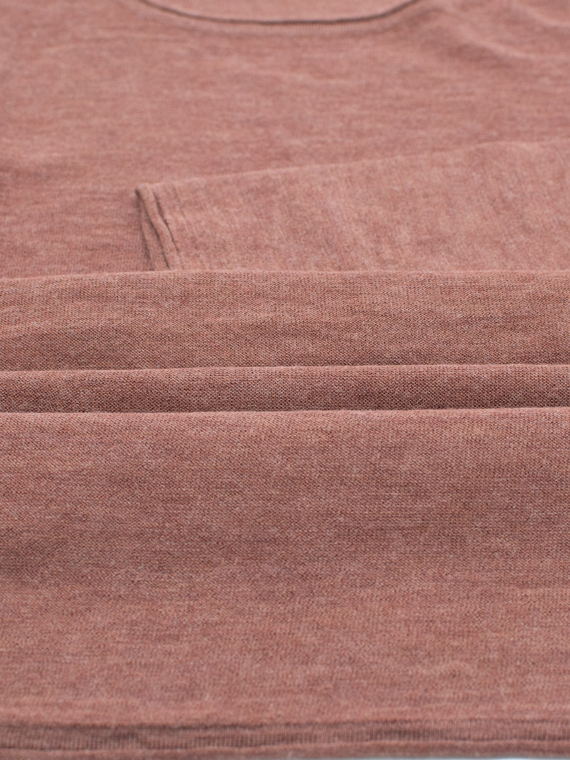 Close-up of a folded, textured brown fabric from the Vogue Lightweight Merino Sweater by ID Menswear. The soft material is neatly arranged, showcasing the reverse knit design that highlights the fibers and subtle color variations.