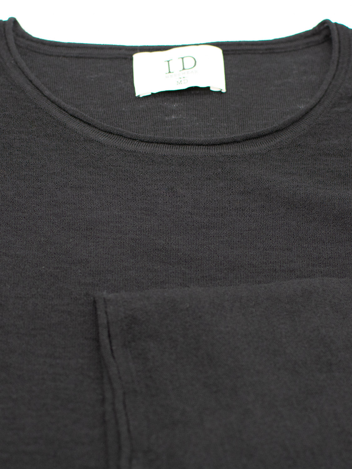 Close-up of the Vogue Lightweight Merino Sweater in black with a round neckline by ID Menswear. Its crafted from extra fine Merino wool, features a small brand tag inside the collar with size info, and has visible stitching near the pocket for added texture.