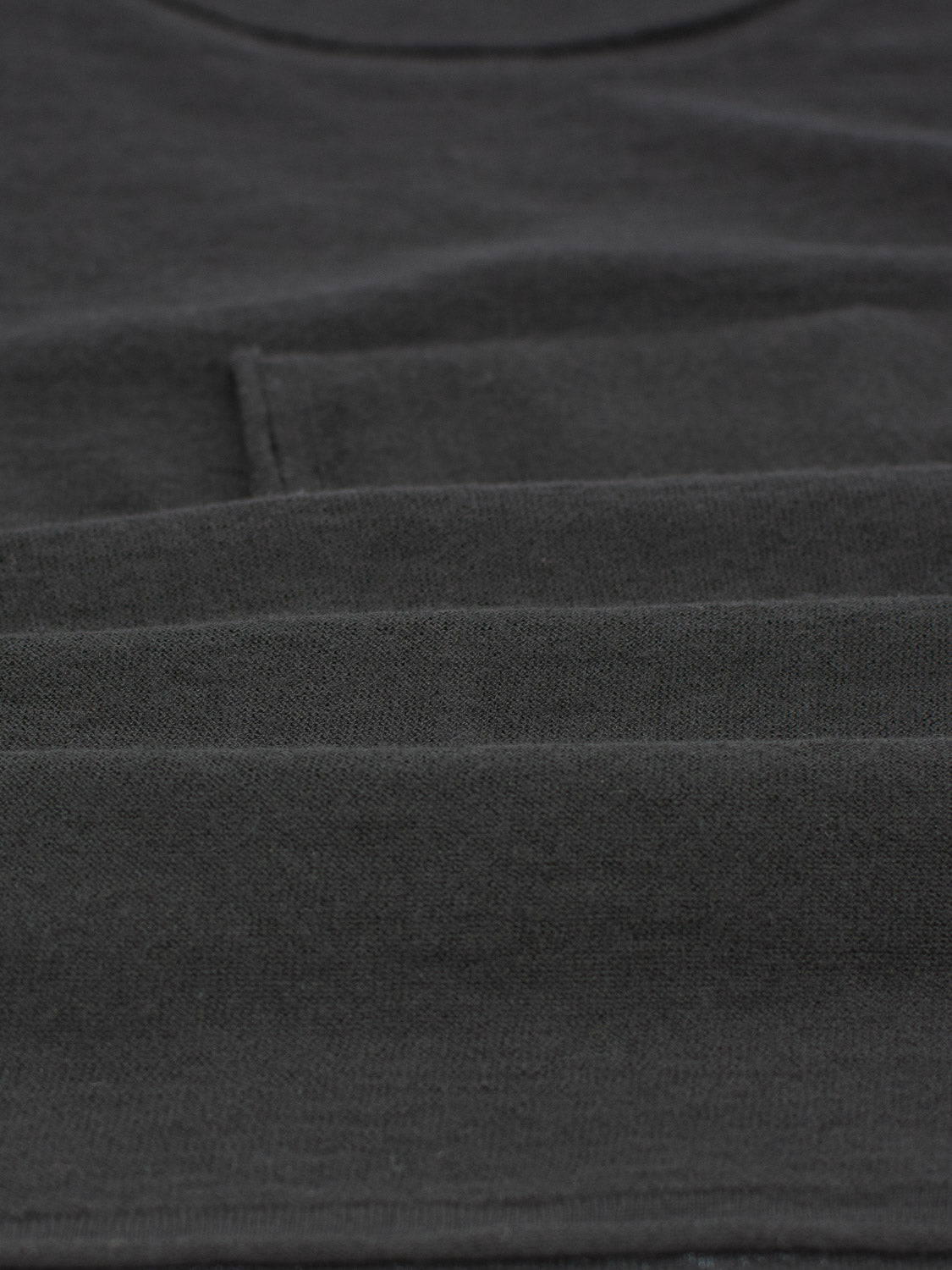 Close-up of a black Vogue Lightweight Merino Sweater by ID Menswear, featuring a curved neckline and layered folds. The texture and fine stitching are showcased in this extra fine Merino wool design.