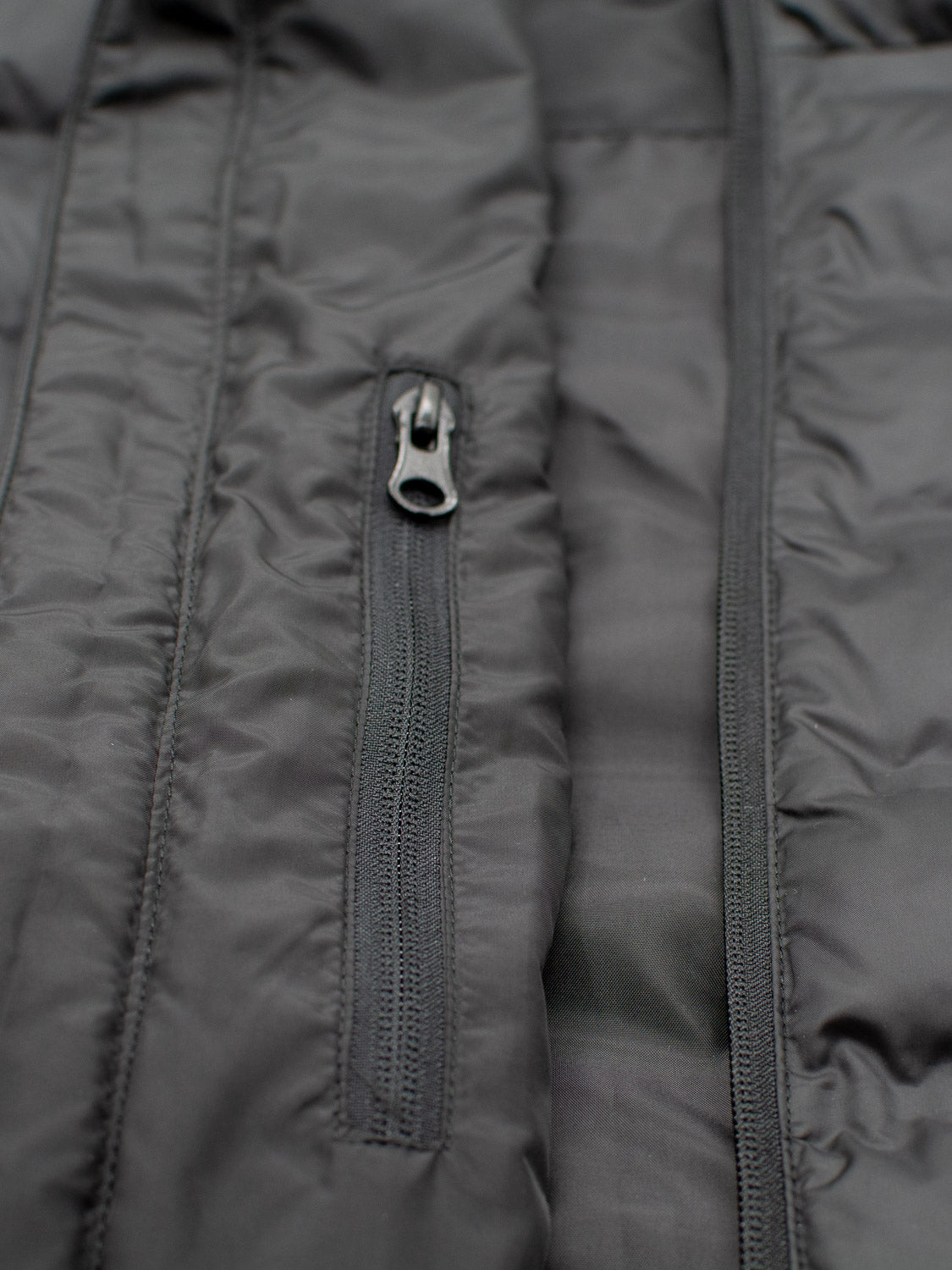 Close-up of the Yukon Hooded Puffer Jacket by ID Menswear featuring a lightweight polyester shell, vertical zippered pocket, detailed stitching, and quilted fabric texture.