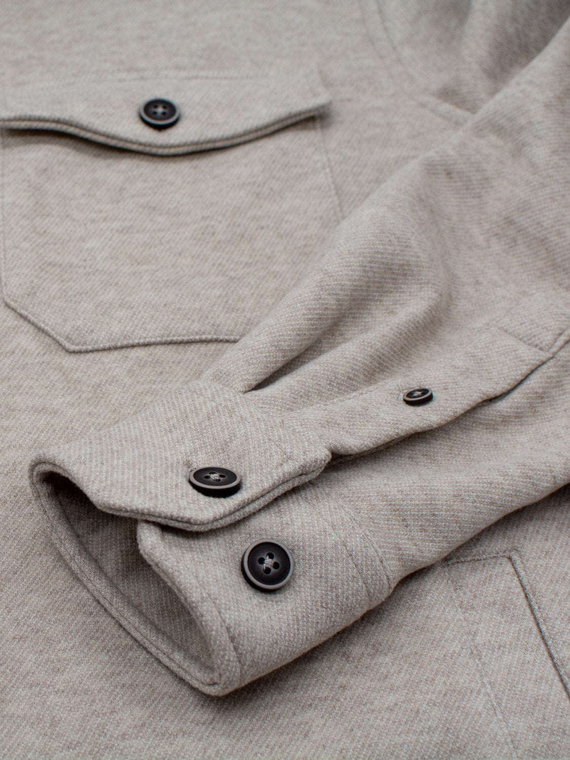 A close-up of ID Menswears beige Yukon Shirt Jacket shows a textured sleeve with two black buttons and a pocket flap with a black button, ideal for casual outings in transitional weather. The fabric appears soft and finely woven.
