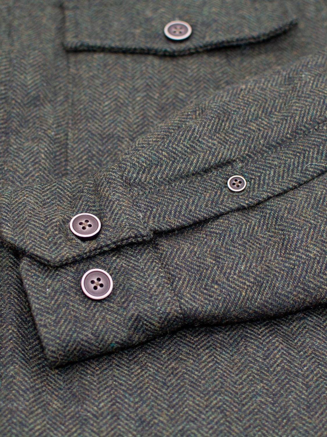 Close-up of the ID Menswear Stuntman Wool Blend Tweed Jacket in textured gray herringbone, featuring a buttoned chest pocket and cuffs—a timeless piece crafted for style and comfort with a subtle zigzag pattern.
