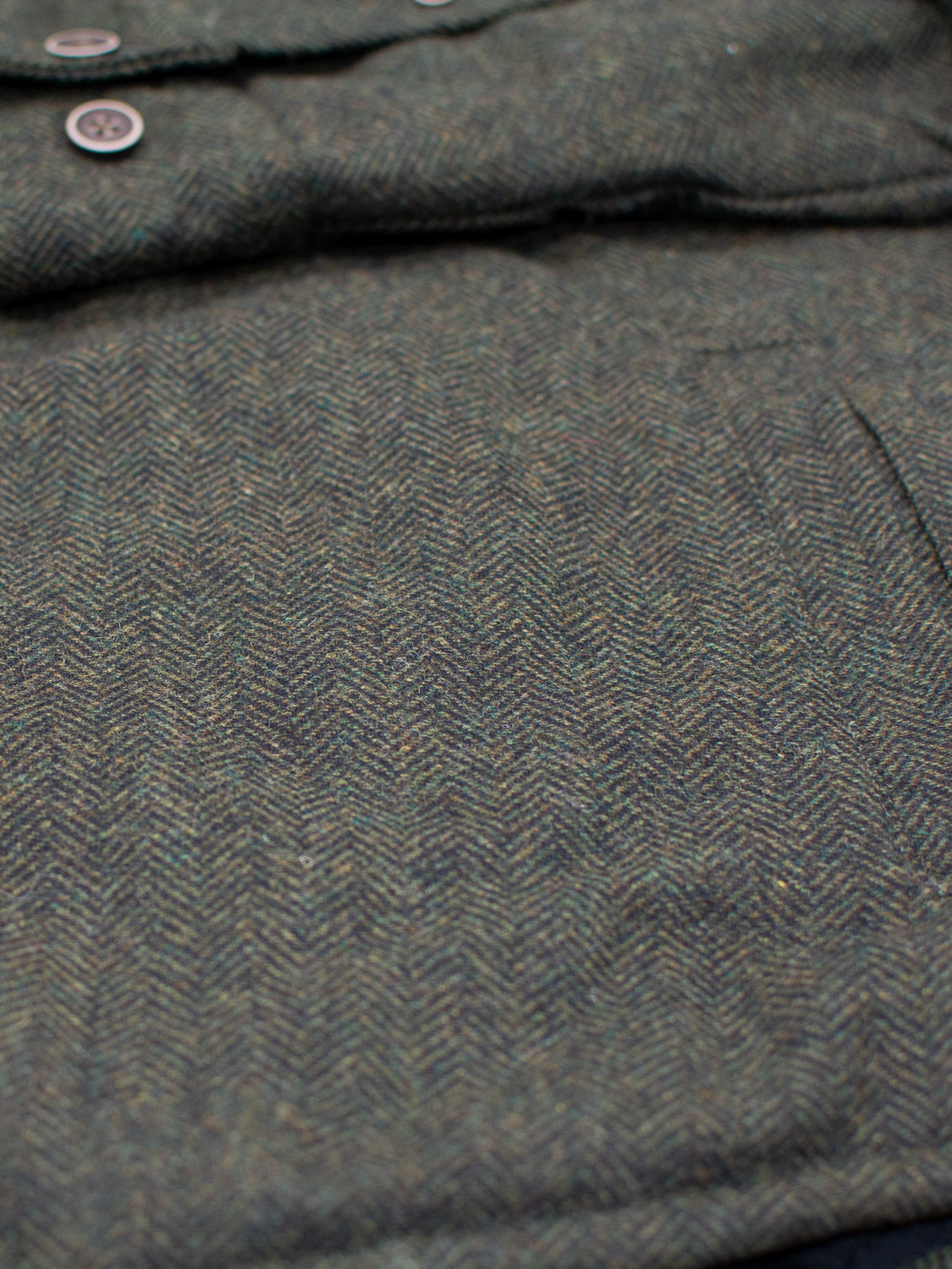 Close-up of the Stuntman Wool Blend Tweed Jacket by ID Menswear, featuring a green and brown herringbone pattern, visible buttons, pocket, and quilted lining—a timeless addition to any wardrobe.